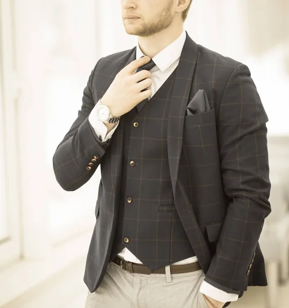 Pensativo iniciante empresário em um terno de negócios fica perto da janela e endireita sua gravata — Fotografia de Stock
