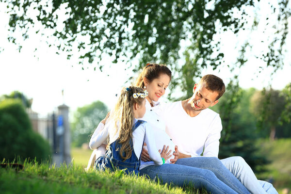 expectant parents and their little daughter sitting on the grass