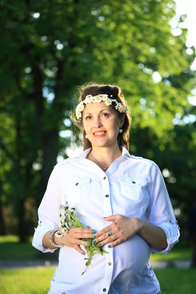 Mujer embarazada feliz en una corona y un ramo de flores silvestres o — Foto de Stock