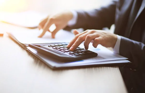 Os empresários contam com a calculadora sentada na mesa. Fechar as mãos e artigos de papelaria — Fotografia de Stock