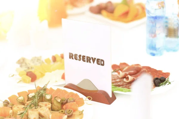 A reserved sign on the restaurant table in bright sunny weather against a background of dishes — Stock Photo, Image