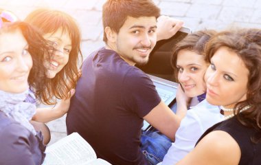 Bir dizüstü bilgisayar güneşli bir günde bir üniversite arka plan ile neşeli öğrenci grubu