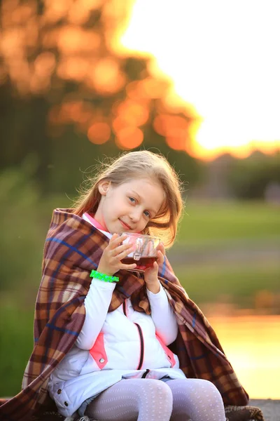 Niña con una taza de cacao caliente envuelta en una manta sentada — Foto de Stock