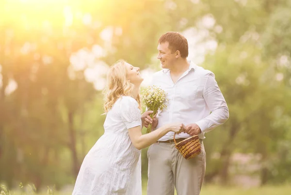Happy couple - pregnant woman and her husband in a park with daisies — Stock Photo, Image