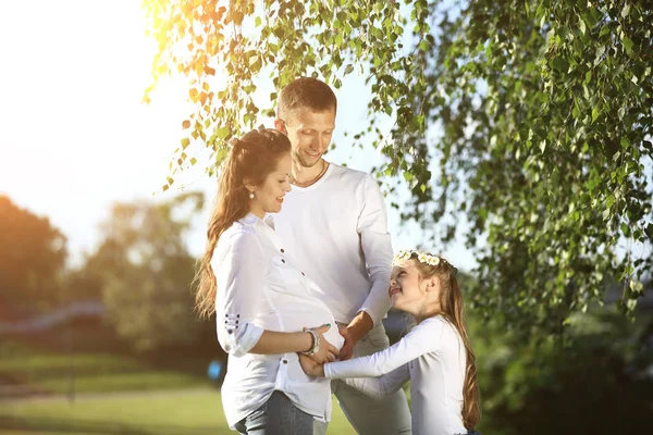 Glücklicher Vater und kleines Mädchen umarmen ihre schwangere Mutter auf einer wa — Stockfoto