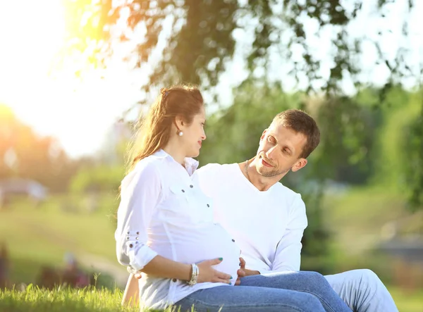 Zukünftige Eltern sitzen an einem sonnigen Tag auf dem Rasen im Park. — Stockfoto