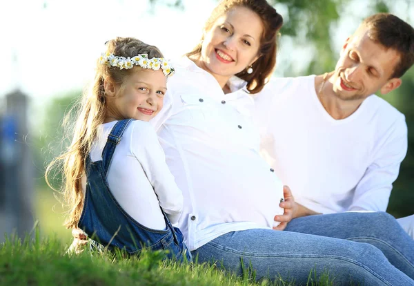 Nastávající rodiče a jejich malá dcera seděla na trávě — Stock fotografie
