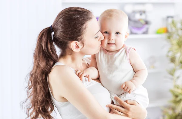 Retrato de uma mãe feliz com um bebê de anos em seus braços no fundo de uma sala de crianças — Fotografia de Stock