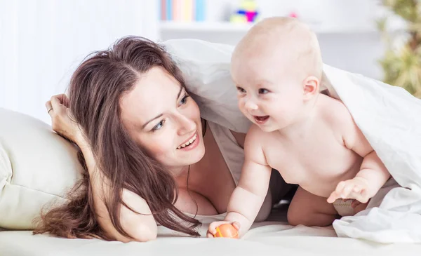 Koncepcja szczęśliwych matek: szczęśliwa matka i jej roczne dziecko bawiące się na kanapie w sypialni — Zdjęcie stockowe