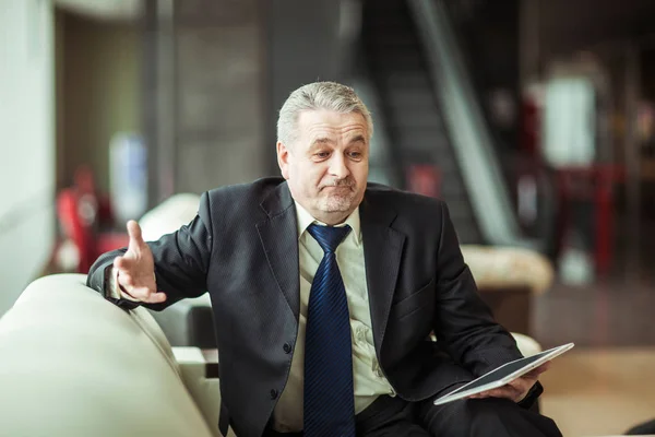 Smiling experienced businessman with digital tablet sitting on sofa in the office — Stock Photo, Image