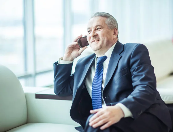 Erfolgreicher Geschäftsmann, der auf dem Sofa im Büro auf seinem Smartphone spricht — Stockfoto