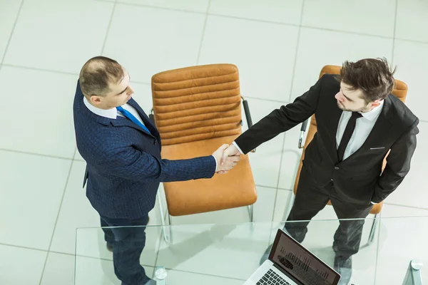Handshake partnerów biznesowych w pobliżu pulpitu, w przestronne biuro — Zdjęcie stockowe