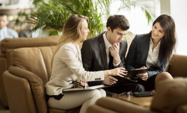 Çalışma kağıtları modern bir ofis lobisinde kanepede oturan tartışırken iş takım