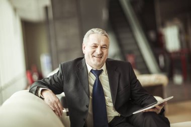 ofis önünde sandalyede oturan dijital tablet ile işadamı portresi.
