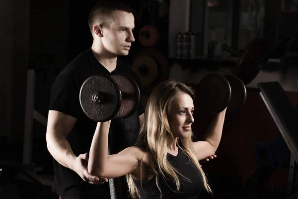 Fitnesstrainerin zeigt der Kundin, wie sie die Übung am Simulator richtig ausführt — Stockfoto