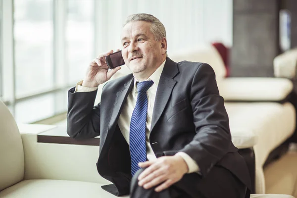 Erfolgreicher Geschäftsmann, der auf dem Sofa im Büro auf seinem Smartphone spricht — Stockfoto