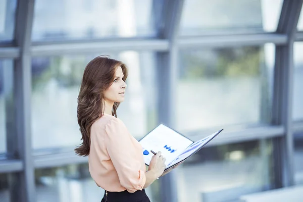 Mulher de negócios bem sucedida com documentos financeiros em pé perto de uma grande janela em um escritório moderno — Fotografia de Stock