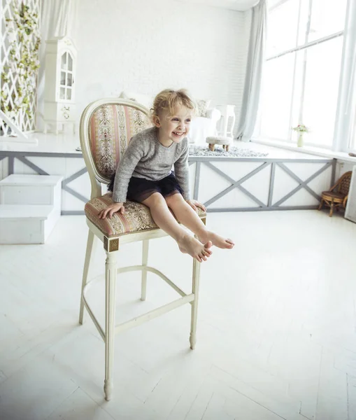 Retrato de una niña feliz de cinco años sentada en una silla en el amplio salón — Foto de Stock