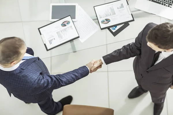 Handshake finansiella partner, på skrivbordsbakgrunden, med finansiella scheman — Stockfoto