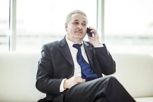 Úspěšný podnikatel, mluví na jeho smartphone sedí na gauči v kanceláři — Stock fotografie