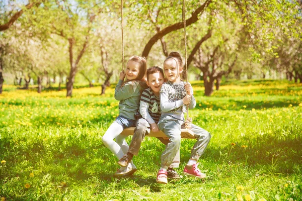 Tres niños pequeños montan en los columpios del parque — Foto de Stock