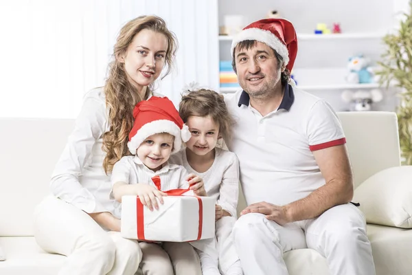 Šťastná rodina s vánoční dárek sedí na pohovce v dětském pokoji. — Stock fotografie