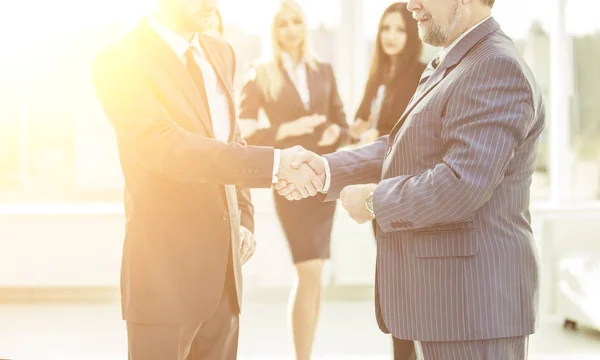 Koncept spolupráce - handshake obchodních partnerů na pozadí zaměstnanců v kanceláři — Stock fotografie