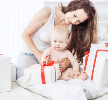 happy mothers her infant baby consider holiday shopping, folded on the sofa in the room clipart