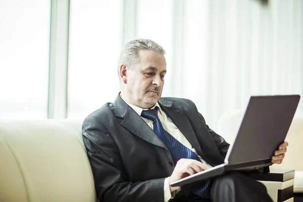 Hombre de negocios experimentado que trabaja en el ordenador portátil sentado en el sofá en una oficina privada —  Fotos de Stock