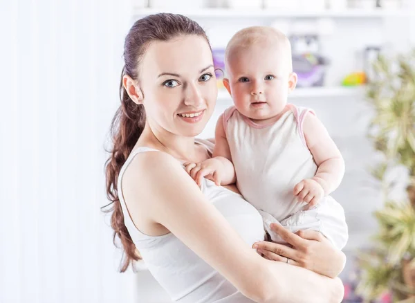 Portret van een gelukkige moeder met een baby van een jaar in haar armen op de achtergrond van een kinderkamer — Stockfoto