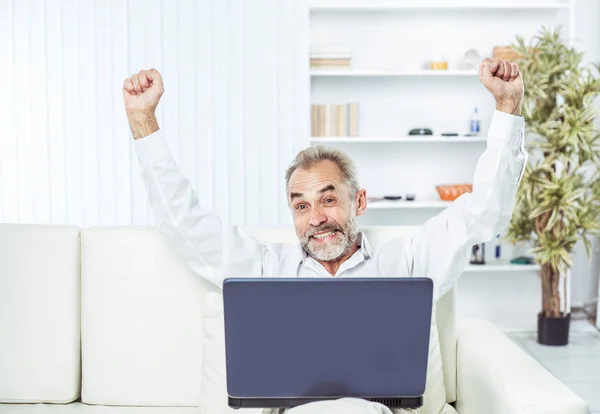 Enthusiastic businessman with an open laptop sitting on sofa in modern office. — Stock Photo, Image