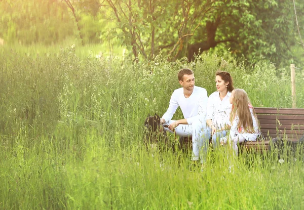 Feliz familia sentada en un banco en el parque en verano Día soleado . — Foto de Stock