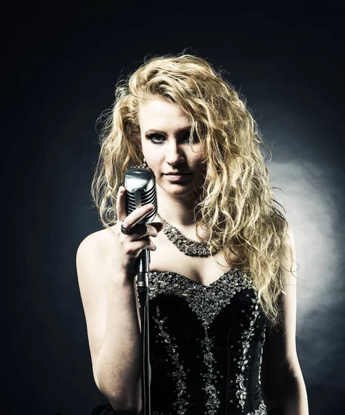 Красивая блондинка певица в черном платье держит микрофон и поет песню . — стоковое фото