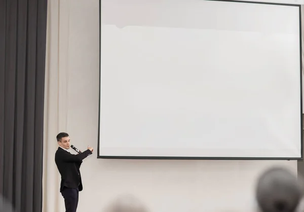 Haut-parleur conduit les travaux de la conférence debout devant un grand écran blanc sur la scène dans la salle de conférence — Photo