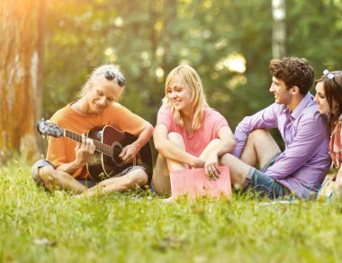 bir grup öğrenci parkta oturan bir gitar ile