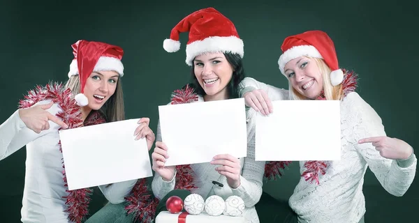 Três meninas no traje de Papai Noel mostrando folha em branco — Fotografia de Stock