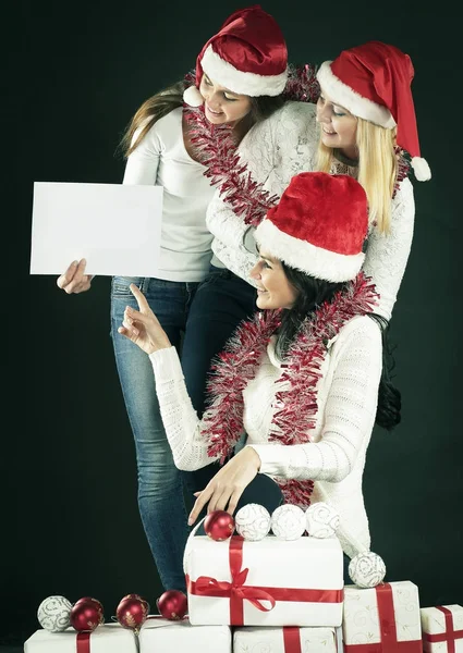 Noel Baba kostümlü üç genç kız boş çarşaf gösteriyor. — Stok fotoğraf