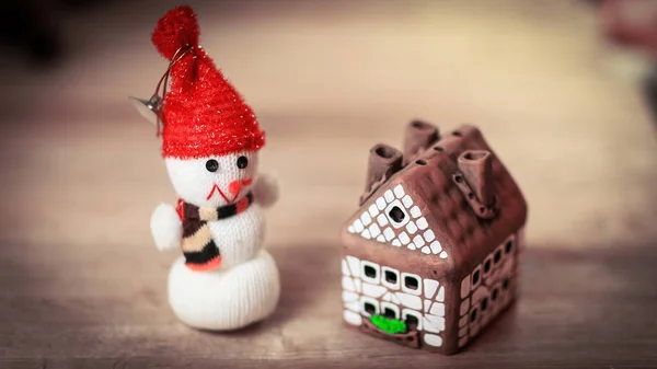 Muñeco de nieve de juguete y casa de jengibre en la mesa de Navidad —  Fotos de Stock