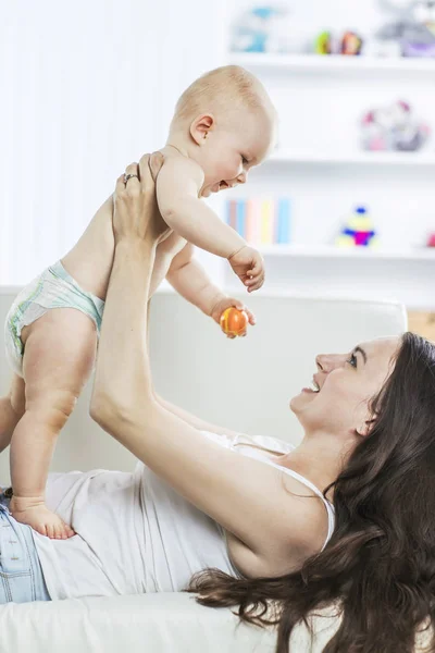 Concepto de felicidad: madre feliz jugando con un bebé de un año en la habitación para los niños — Foto de Stock