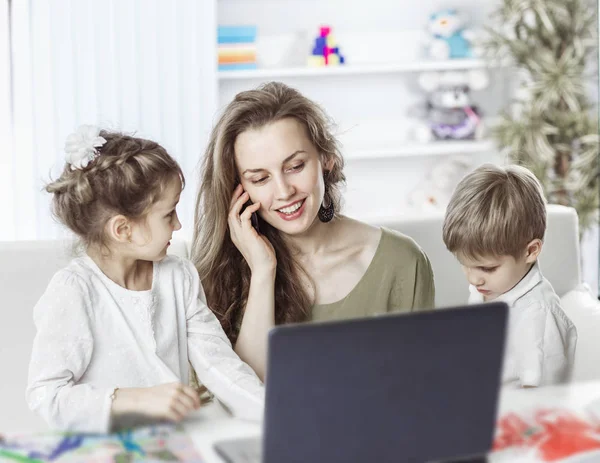 Joven madre - mujer de negocios trabajando en el ordenador portátil y hablando en el teléfono inteligente junto a sus hijos — Foto de Stock