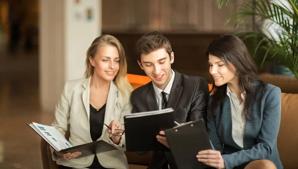 Business team discussing working papers sitting on the couch in the lobby of a modern office — Stock Photo, Image