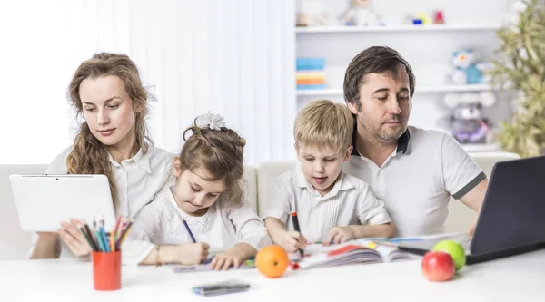 Mamma e papà che comunicano su Internet, e la figlia e il figlio disegnano, seduti a tavola nella nursery — Foto Stock