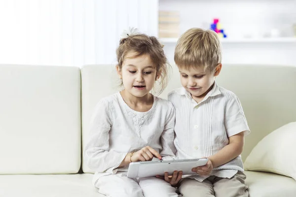 Mały brat i siostra z cyfrowego tabletu siedzi na kanapie w przedszkolu. — Zdjęcie stockowe