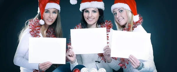 Trzy młode dziewczyny w stroju Świętego Mikołaja Wyświetlono pusty arkusz — Zdjęcie stockowe