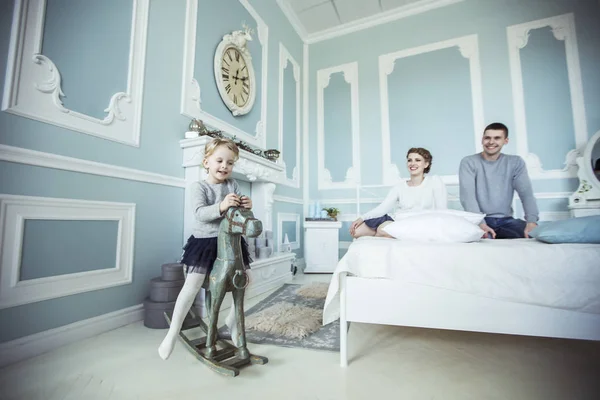 Menina balançando em um cavalo de madeira no quarto de seus pais — Fotografia de Stock