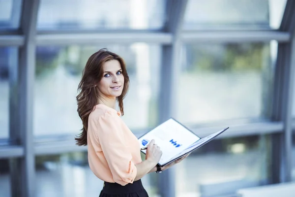 Femme d'affaires prospère avec des documents financiers debout près d'une grande fenêtre dans un bureau moderne — Photo