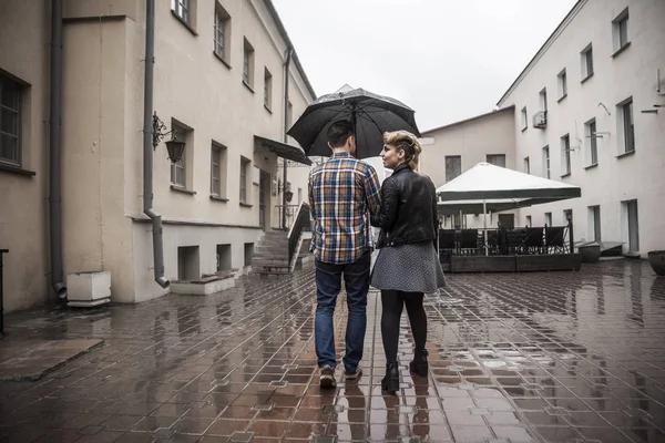 Feliz pareja amorosa está bajo un paraguas en una calle de la ciudad en un día lluvioso — Foto de Stock