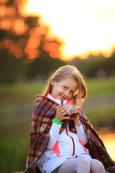 Niña con una taza de cacao caliente envuelta en una manta sentada — Foto de Stock