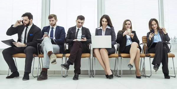 Бизнес-команда ищет информацию в Интернете с помощью смартфона и ноутбука, сидя в фойе современного офиса — стоковое фото