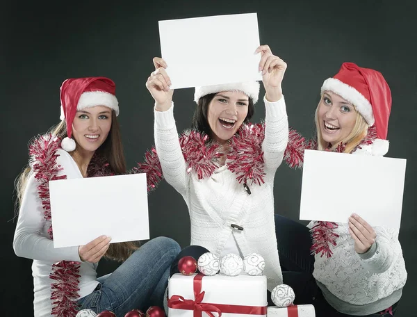 Três meninas no traje de Papai Noel mostrando folhas em branco — Fotografia de Stock